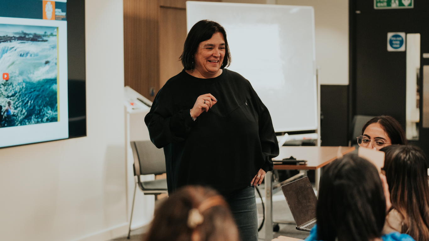 Lecturer presenting in an International Business Management class with students seated and a screen showing ocean waves