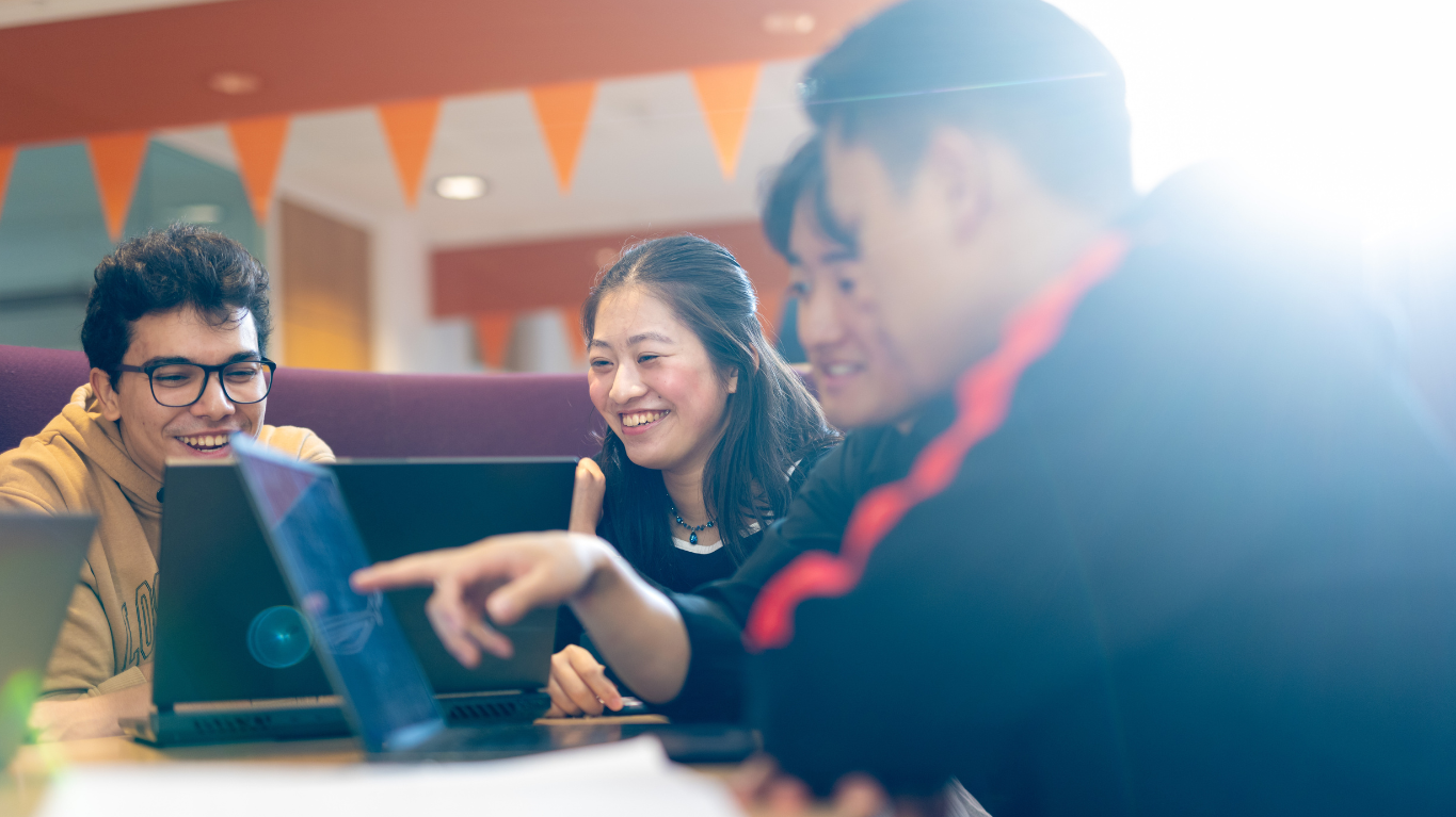 Four students sitting around a table, working on laptops and discussing together.